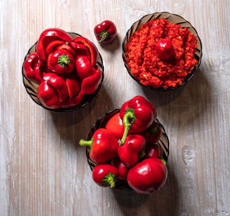 Red peppers and a bowl with homemade adjika on a wooden tableの写真素材