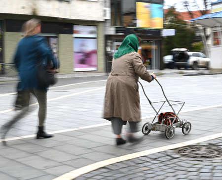 Old woman with cart on the street of the city in motion blur. Defocused imageの写真素材