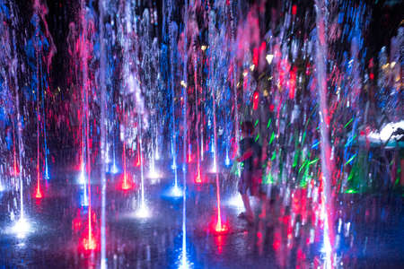Happy children playing in a water fountain in evening lights in motion blur. Defocused imageの写真素材