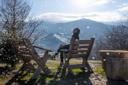 Young woman sitting in lounge chair in mountains on winter dayの写真素材