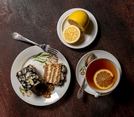 Sweet piece of cake and cup of hot tea with lemon on a wooden tableの写真素材