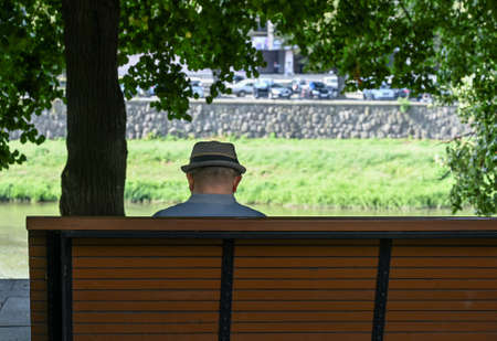 Man in hat sitting alone on bench in beautiful green parkの写真素材