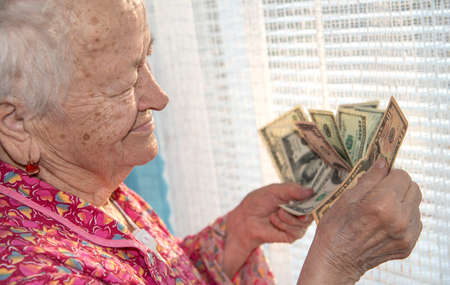 Old woman holding dollar cash money at home