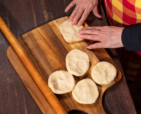 Cooking and home concept. Senior woman preparing tasty pies in the kitchen at homeの写真素材
