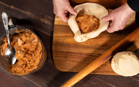 Cooking and home concept. Woman preparing homemade pies with mincemeat filling on the kitchen table at homeの写真素材