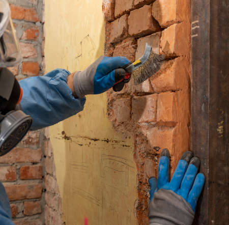 Worker in uniform reconstructing old brick wall. Old house reconstruction, repair