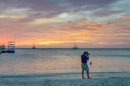 Aruba, Caribbean - September 25, 2012: Photographer at the Sunset with anchored sail boats on sea by the bay. The image was taken in Aruba, in the Caribbean Sea.のeditorial素材