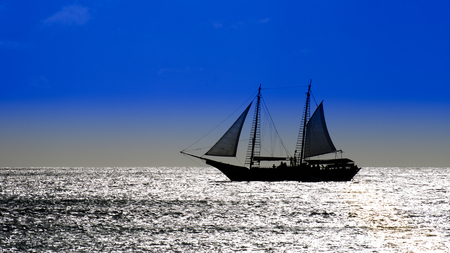 Picture showing a sailboat on sea navigating towards the sunset. The image was taken in the Caribbean Sea.の写真素材
