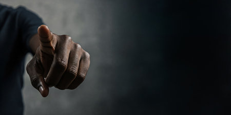 Close-up of a Black man's hand pointing directly at the camera with focus on the finger against a dark backgroundの素材