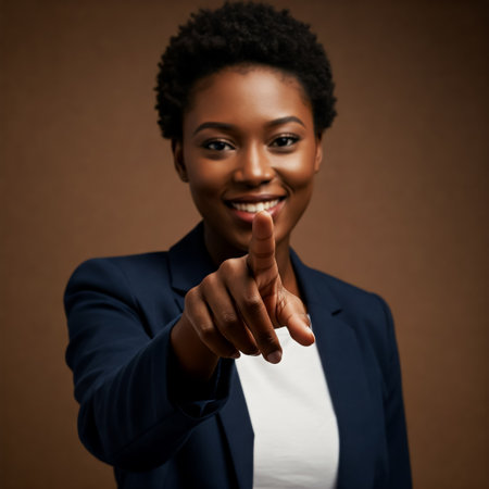Confident Black woman smiling and pointing forward while wearing a navy blue blazer, standing against a neutral brown background indoorsの素材
