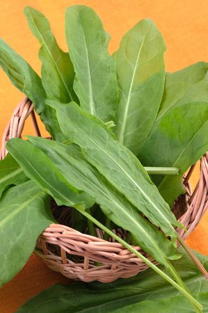 Sorrel leaves in a basket on an orange cloth.