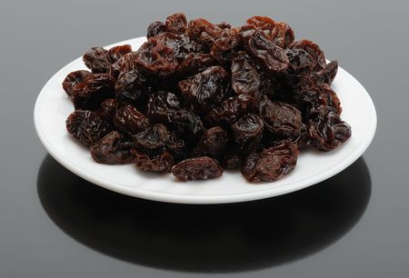 Big brown raisins on a white plate on a black backgroundの写真素材