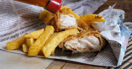 Adding vinegar on an English fish and chips wrapped in newspaper, the traditional wayの写真素材