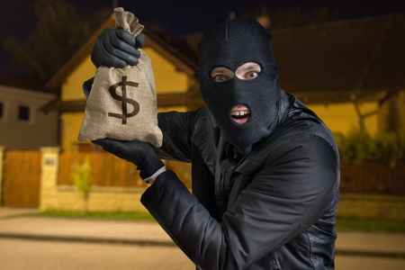 Happy robber or burglar is showing stolen bag full of money at night.