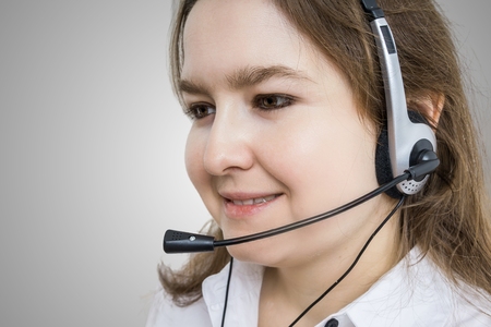 Telemarketing and customer service concept. Young smiling woman - operator on gray background.の写真素材