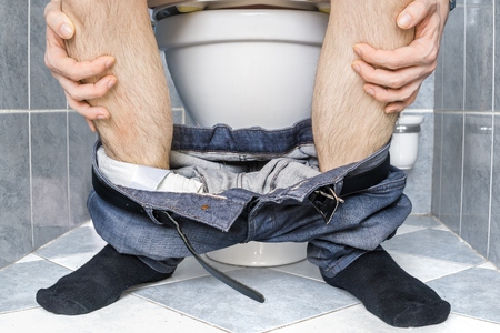 Legs of man with diarrhea who is sitting on toilet.