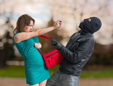 Self defense concept. Young woman is spraying with pepper spray on thief.の写真素材