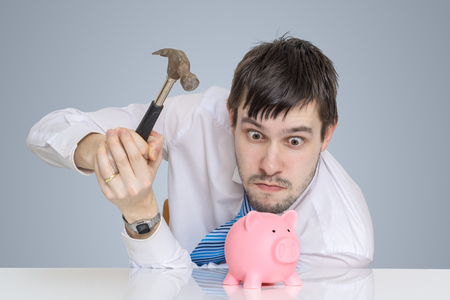 Young man is breaking piggy money bank with hammer to take his savings.の写真素材