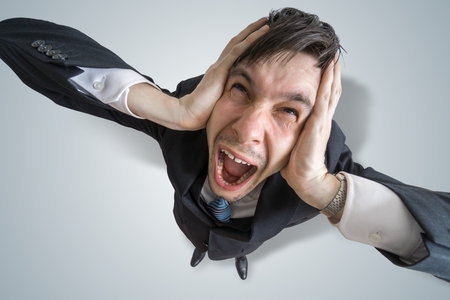 Young schizophrenic man suffers from headache and covering his ears with hands.
