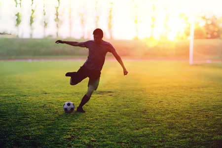 Soccer player is shooting a ball in stadium at sunset.の写真素材