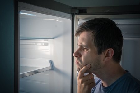 Hungry man is looking for food in empty fridge at night.の写真素材
