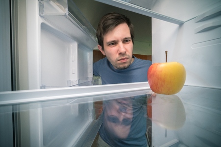 Hungry man is looking for food in fridge. Only apple is inside empty fridge.の写真素材