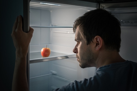 Hungry man is looking for food in fridge at night. Only apple is inside empty fridge.の写真素材