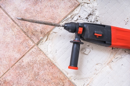 Removing old tiles. Jackhammer - drilling demolition hammer on floor.