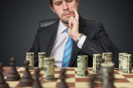 Investment strategy concept. Man is playing chess with money.の写真素材