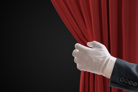 Actor is pulling red curtains in theatre with hand.の写真素材