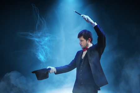 Magician or illusionist is showing magic trick. Blue stage light in background.の写真素材