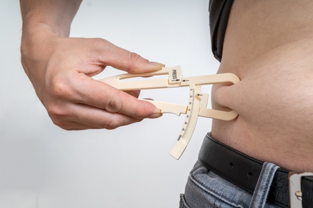 Man is measuring body fat on his belly with caliper.の写真素材