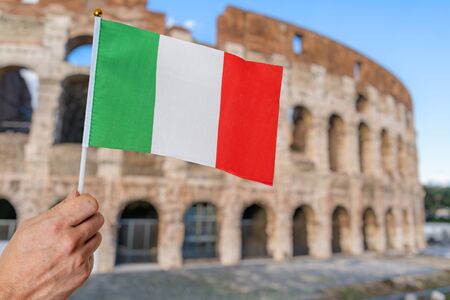 Man is holding italian flag in hand. Colosseum in background. Travel in italy concept.の写真素材