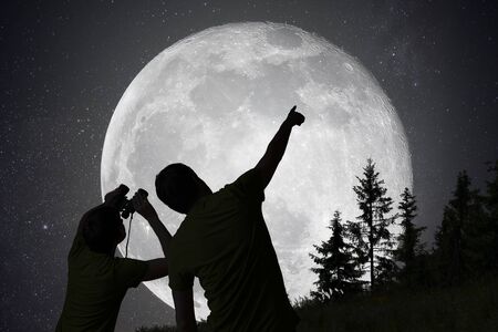 Silhouettes of people observing stars in night sky. Moon in background.の写真素材