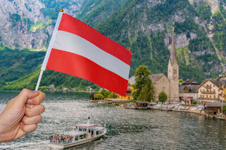 Tourist is holding austrian flag in Hallstatt in Austria. Travel concept.
