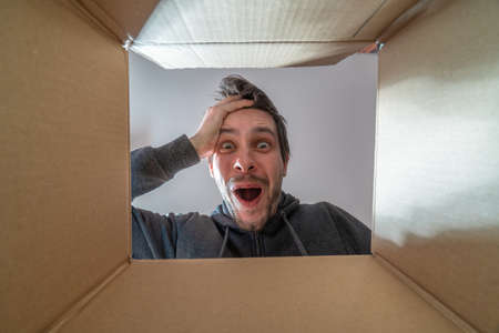 Happy and surprised man is opening a gift and looking inside cardboard box.の写真素材