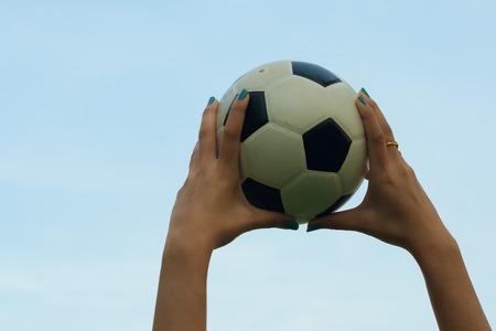 Woman holding a soccer ball up into the sky backgroundの写真素材