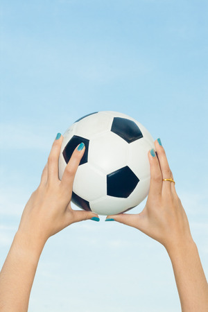 Woman holding a soccer ball up into the sky backgroundの写真素材