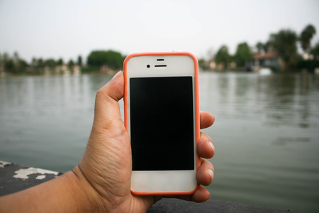 hand held mobile phone beside lake backgroundの写真素材