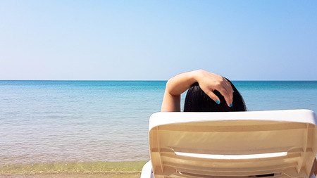 Woman lay on white plastic armchair on the wet beach in hot sunny time with shadow beside the blue...