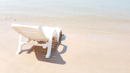 White plastic armchair on the wet beach in hot sunny time with shadow beside the blue seaの写真素材
