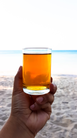 man's hand hold a glass of longan juice above the sand beachの写真素材
