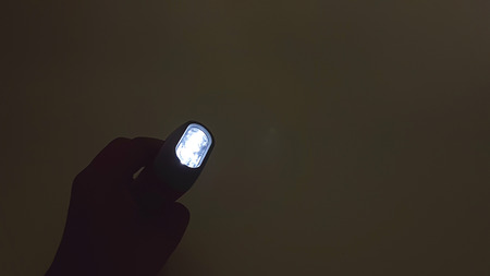 Hand pressing LED flashlight red plastic holder with hand rope isolated