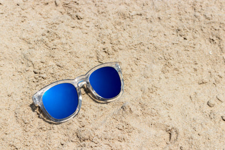 Sun glasses with transparent cover on the sand beach with blue sky backgroundの写真素材