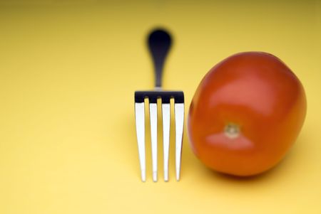 snappy image of a fork and a tomato on a bright yellow backgroundの写真素材