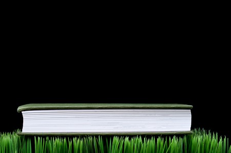 Green hardcover book sitting on grass with a black background and space for copyの写真素材