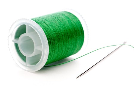 Horizontal extreme closeup of a spool of green thread and a needle