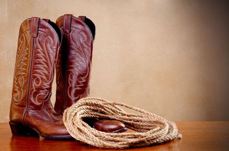 a horizontal image of a pair of brown cowboy boots and a coil of rope on a wooded surface with an old textured backgroundの写真素材