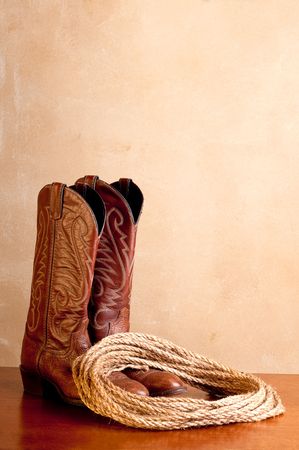 a vertical image of a pair of brown cowboy boots and a coil of rope on a wooded surface with an old textured backgroundの写真素材