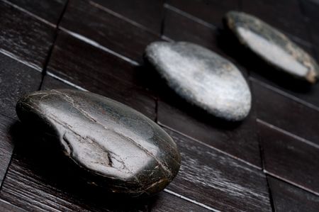 Tilted horizontal shallow focus image of 3 river rocks on black woodの写真素材